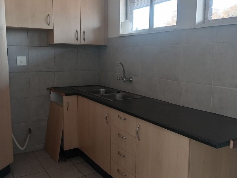A functional kitchen space featuring light wood-finish cabinetry, a double bowl sink, tiled backsplash, and tiled flooring, currently requiring minor repairs to cabinetry.