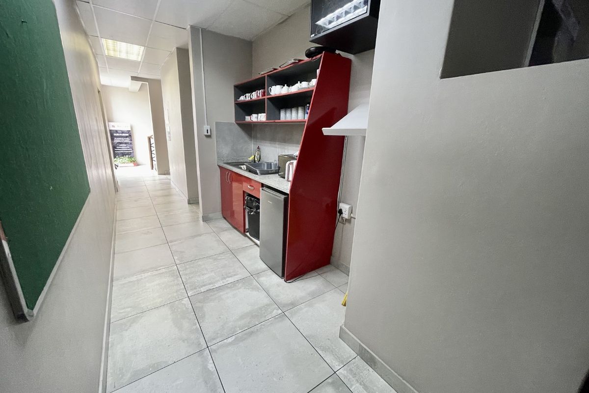 A compact kitchenette area featuring built-in red cabinetry, a stainless steel sink, and tiled flooring within an industrial office corridor.