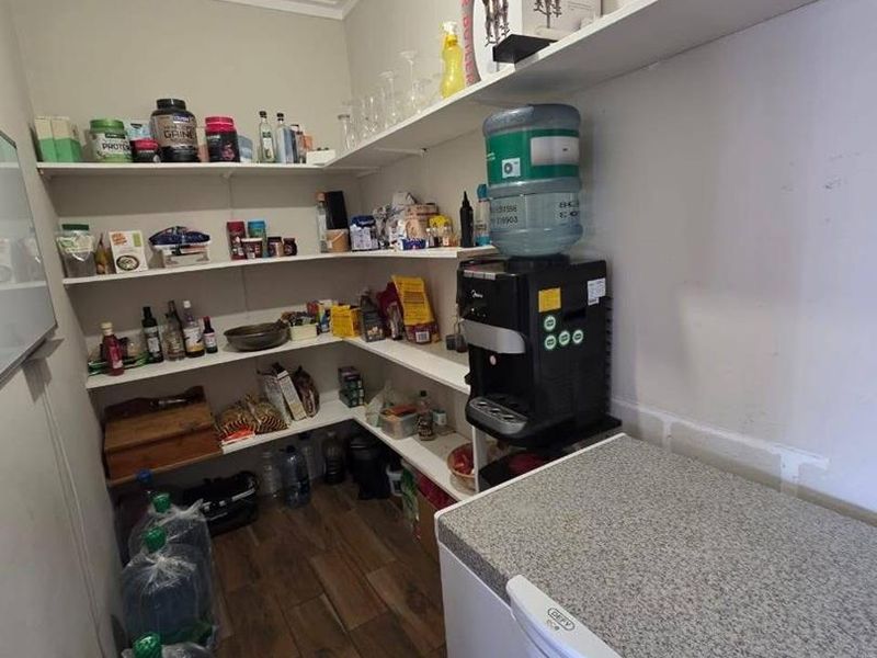 A functional scullery or pantry area featuring extensive built-in shelving and durable laminate flooring, providing ample storage space for household supplies.