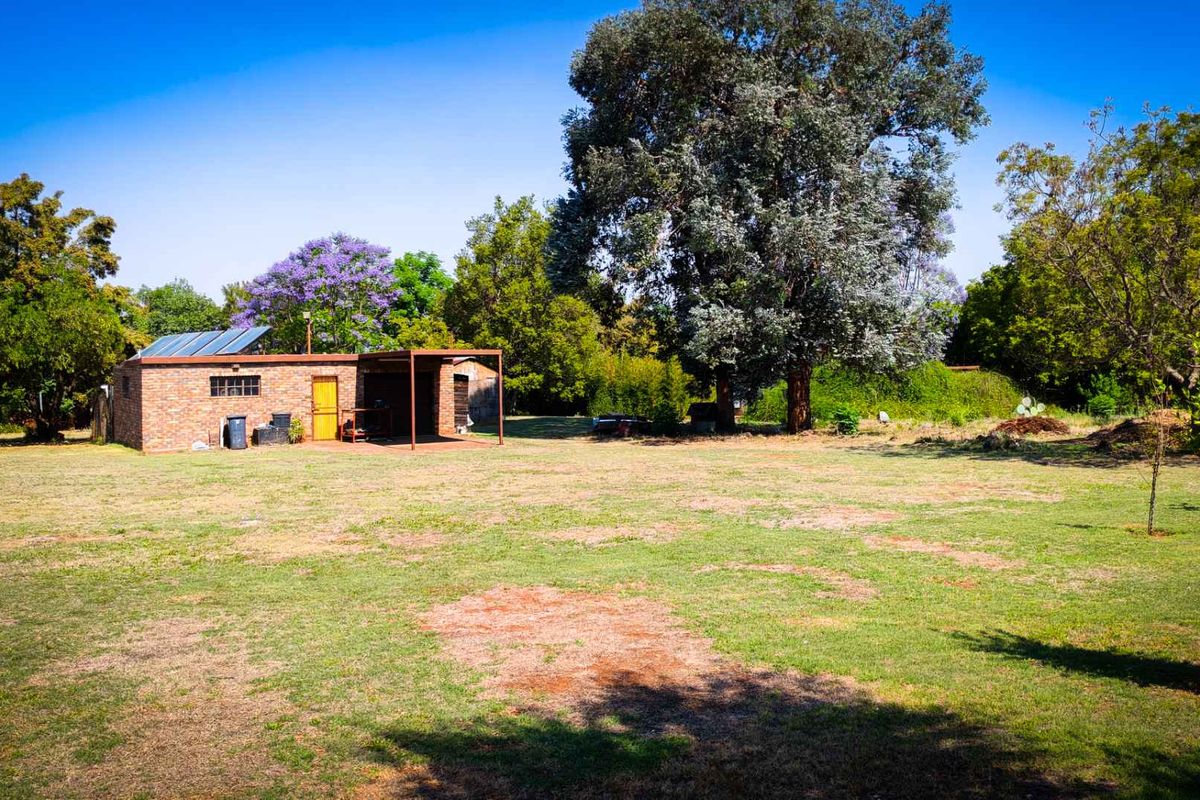 A view of the property grounds featuring a brick outbuilding with a solar geyser installation and a covered patio area set in a spacious garden.