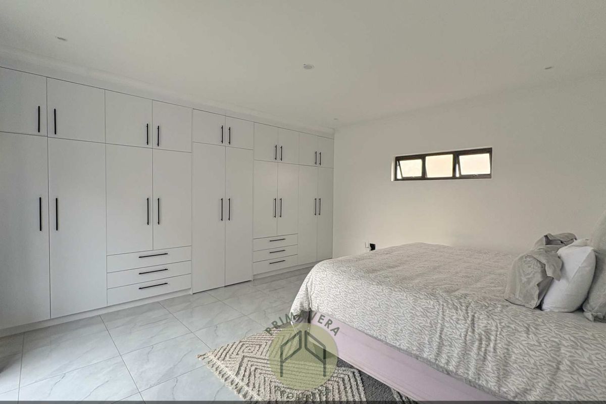 A bright, modern bedroom featuring extensive white built-in cabinetry, sleek tiled flooring, and recessed ceiling lighting.