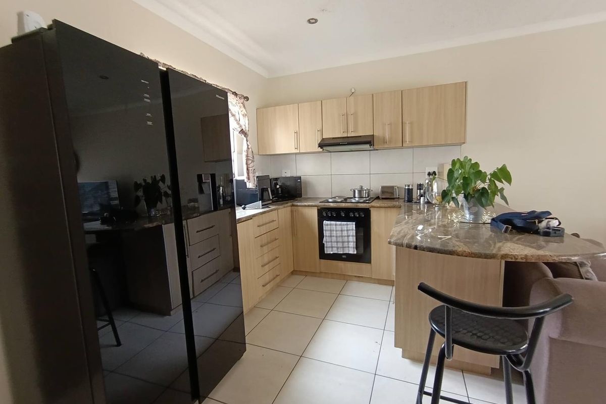 Compact kitchen featuring light wood cabinetry, stone-look countertops, built-in oven, extractor fan, and tiled flooring, integrated into an open-plan living space.