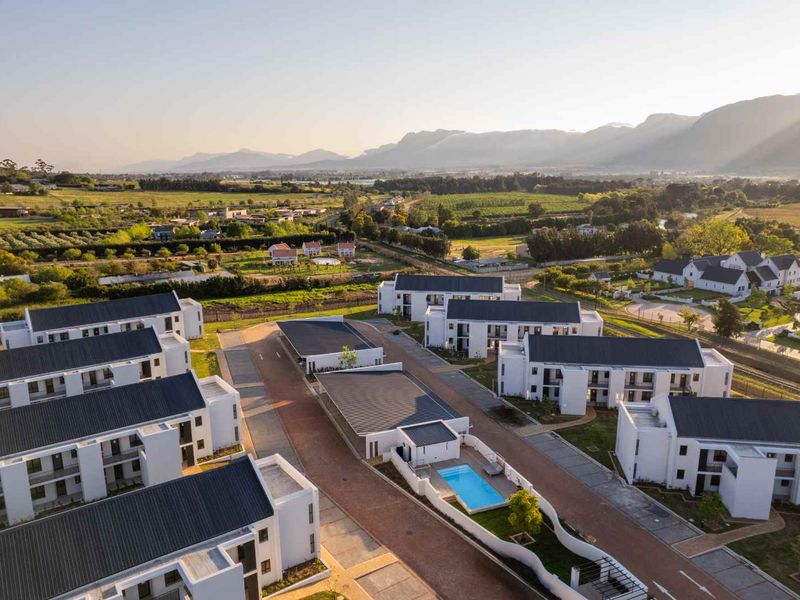 Aerial view of a modern apartment complex featuring white buildings with dark pitched roofs, paved driveways, and a communal swimming pool.