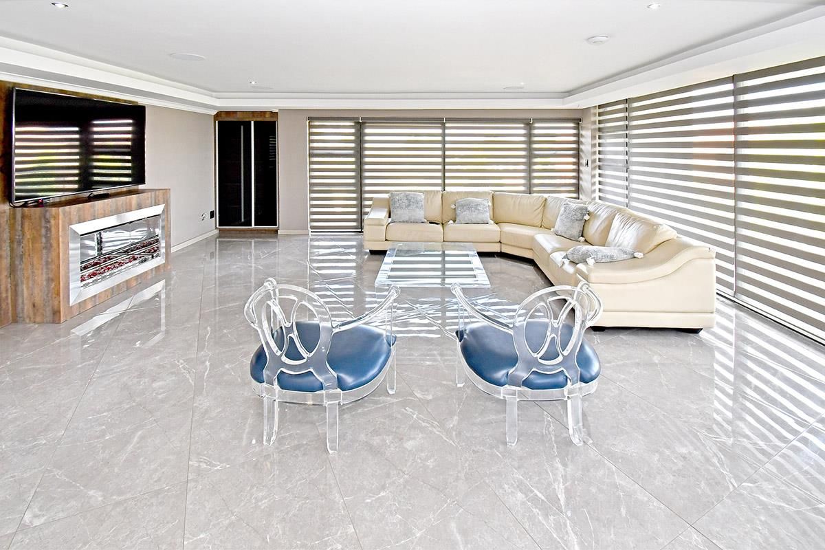 Spacious modern living room featuring large format polished marble-look floor tiles, a built-in fireplace, recessed ceiling lighting, and expansive windows with fitted blinds.