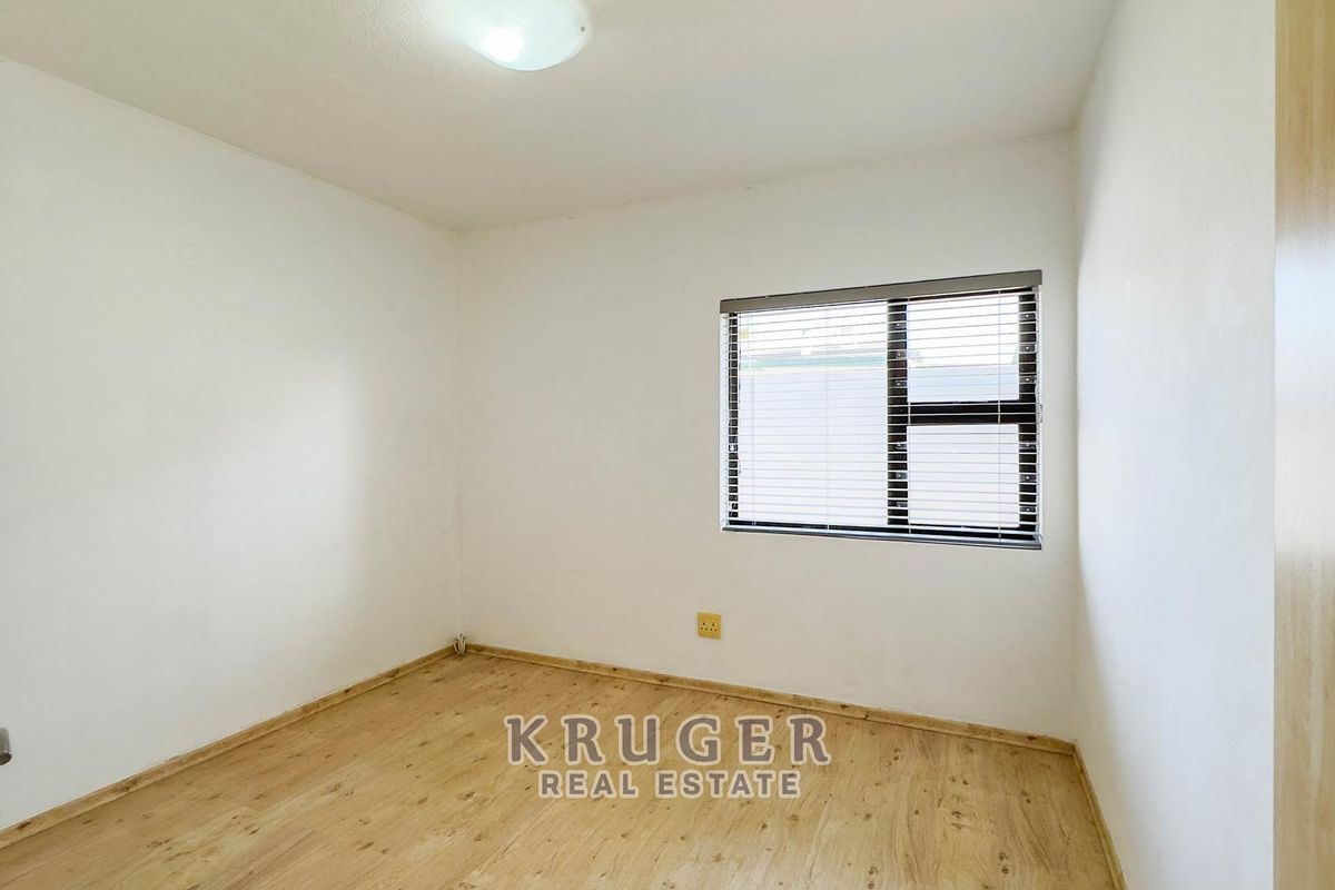 A clean, empty bedroom featuring light-toned laminate flooring, a built-in cupboard, and a window fitted with venetian blinds.