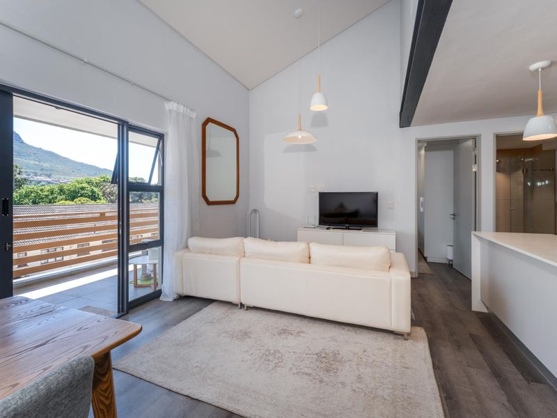 Bright open-plan living area featuring vaulted ceilings, modern laminate flooring, and seamless access to a private balcony with scenic mountain views.