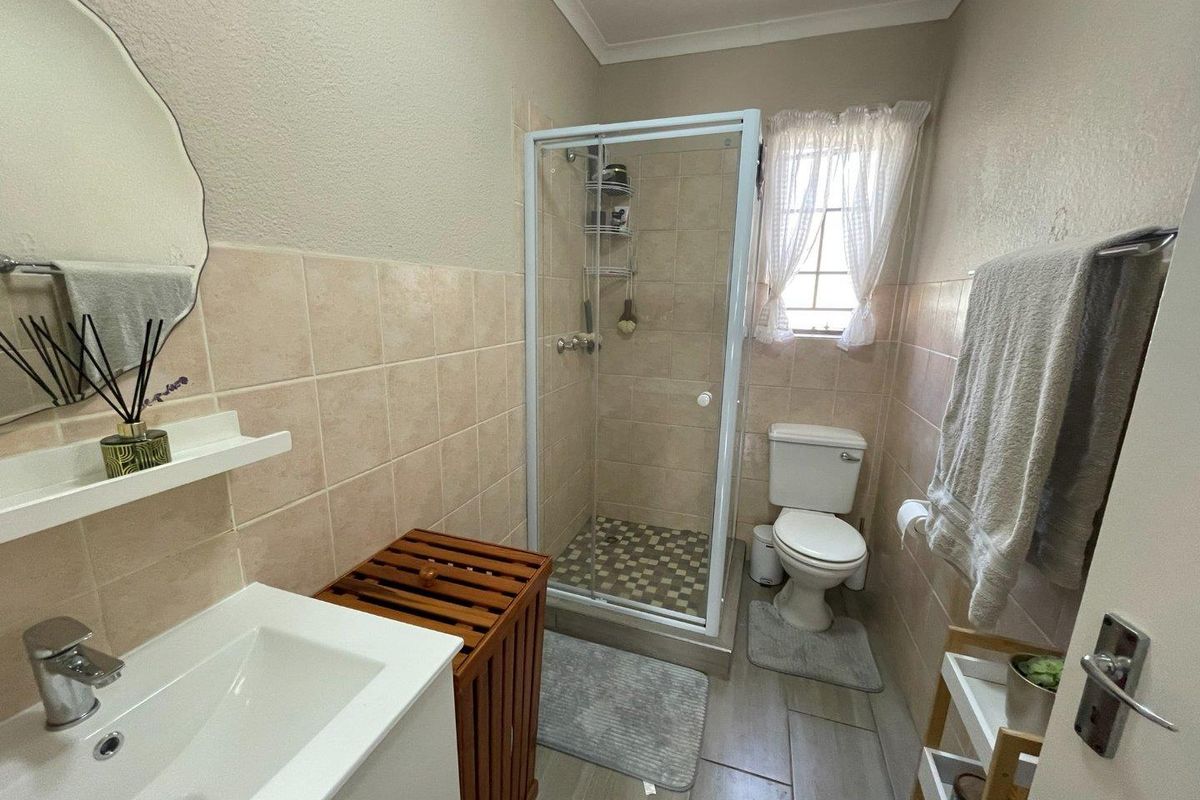 A compact bathroom featuring a glass-enclosed shower, a pedestal vanity with basin, and a standard toilet with neutral wall tiling.