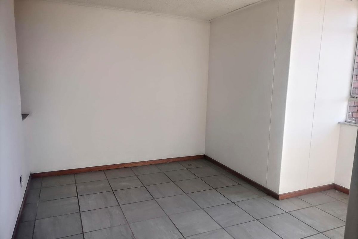 An empty bedroom featuring grey tiled flooring, timber skirting boards, and plain white walls, offering a blank canvas for renovation or interior design.