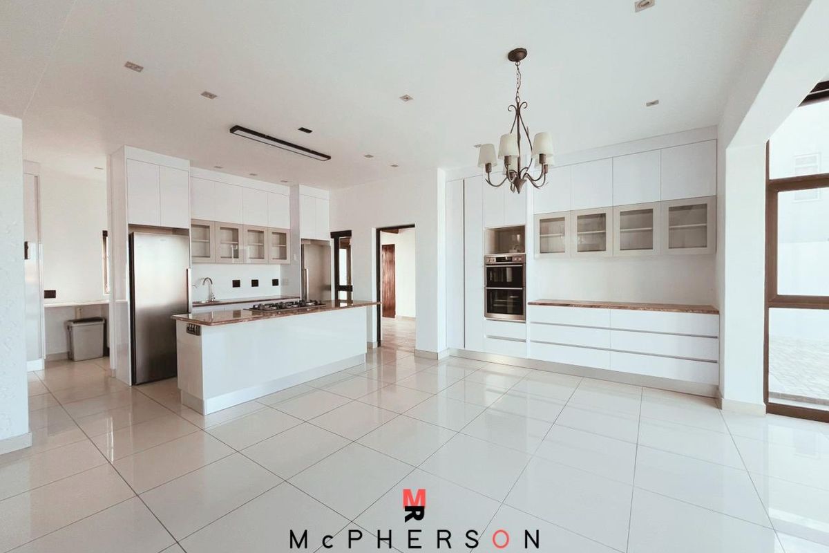 Modern open-plan kitchen featuring sleek white cabinetry, stone countertops, integrated oven, and a central island with a built-in gas hob.