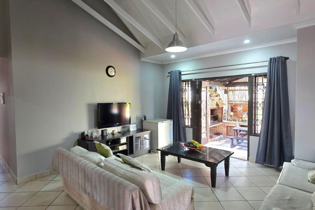 Spacious living room featuring vaulted ceilings, tiled flooring, and large sliding glass doors that provide seamless access to the outdoor patio area.