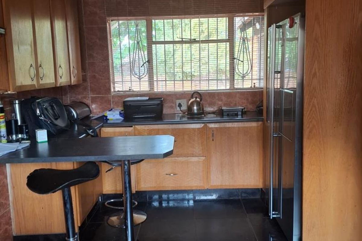 A functional kitchen featuring wood-veneer cabinetry, dark tiled flooring, a breakfast bar, and a window with security bars.
