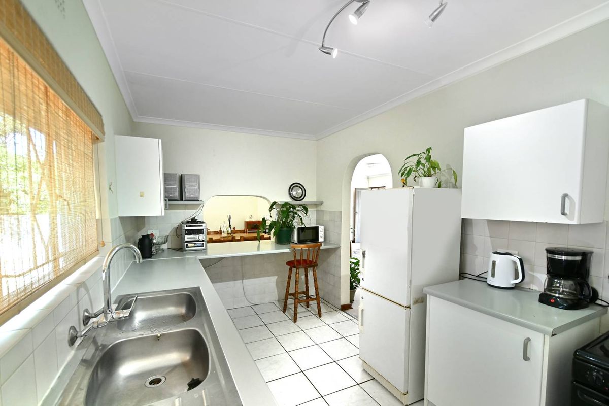 Functional kitchen featuring white cabinetry, double stainless steel sink, tiled flooring, and a convenient breakfast bar pass-through window.