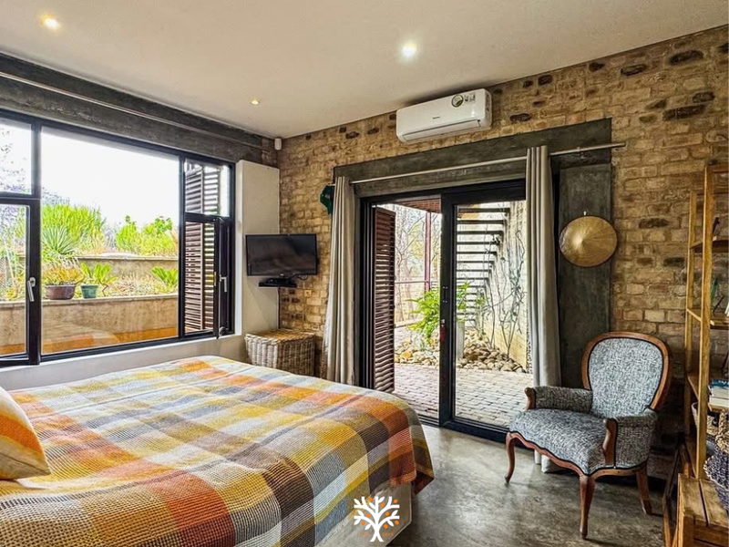 A well-lit bedroom featuring exposed brick walls, polished concrete floors, and direct access to an outdoor patio through sliding glass doors.