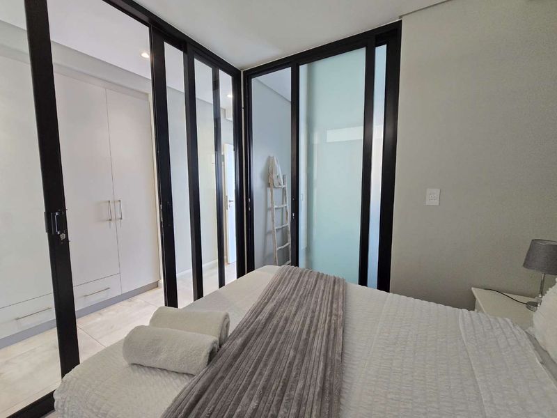 Modern bedroom featuring sleek black-framed sliding glass doors, built-in cupboards, and neutral tiled flooring, creating a contemporary and well-lit living space.