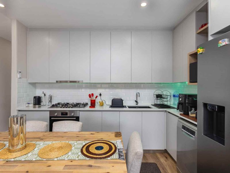 Modern kitchen featuring sleek grey cabinetry, subway tile backsplash, gas hob, built-in oven, and integrated sink, offering a clean and functional culinary space.