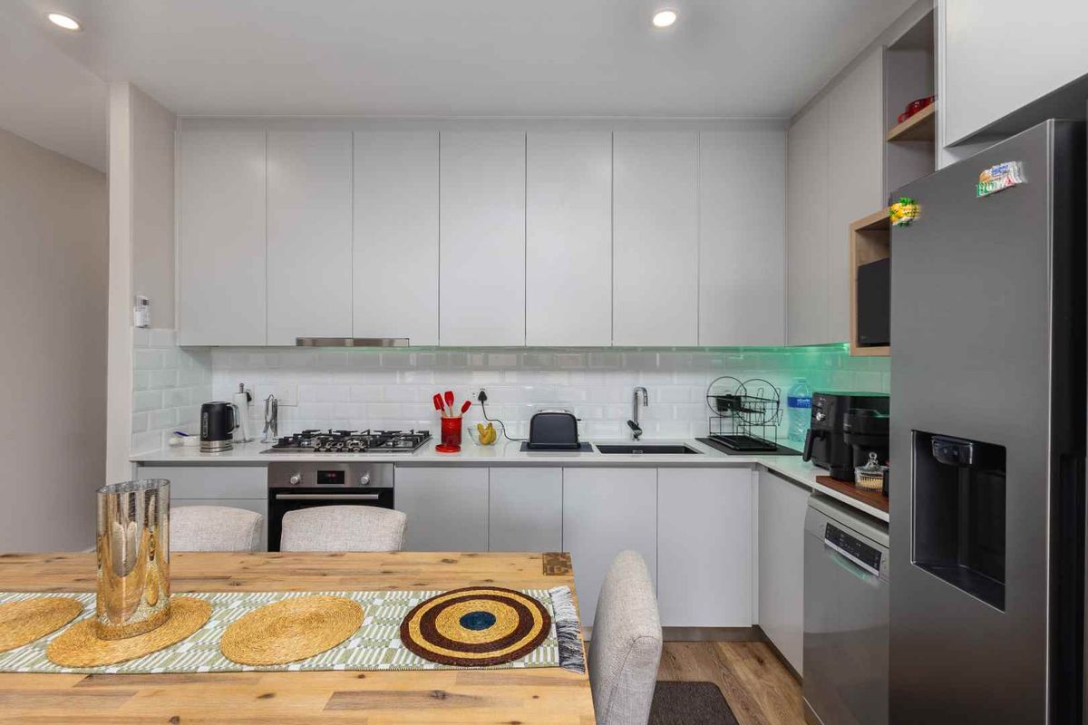Modern kitchen featuring sleek grey cabinetry, subway tile backsplash, gas hob, built-in oven, and integrated sink, offering a clean and functional culinary space.