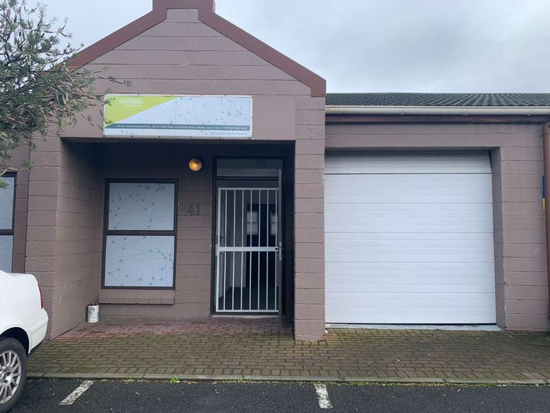 Front elevation of a commercial unit featuring a sectional garage door, secure entrance with security gate, and paved driveway access.