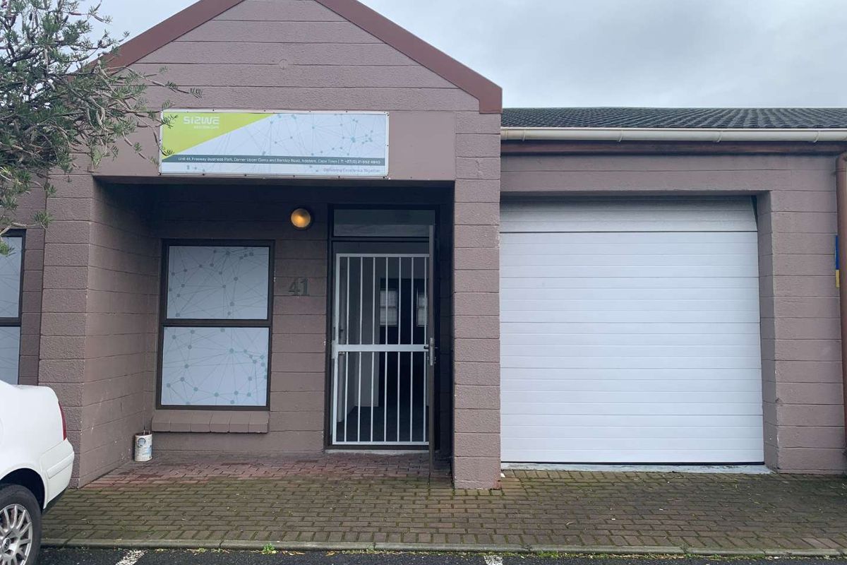 Front elevation of a commercial unit featuring a sectional garage door, secure entrance with security gate, and paved driveway access.