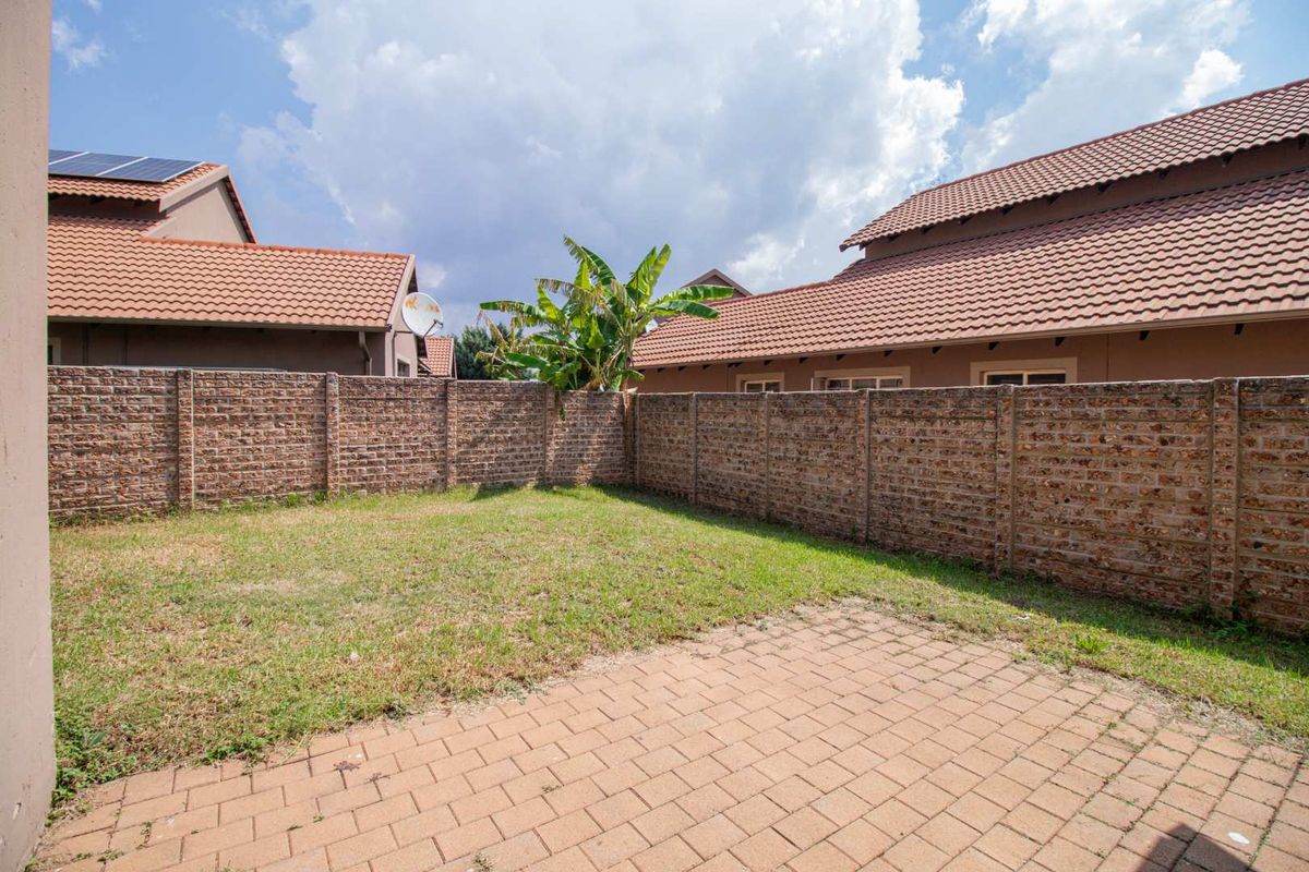 A private rear garden featuring a paved patio area and a grass lawn, enclosed by a high brick boundary wall.