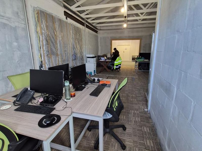 An industrial-style office space featuring exposed roof trusses, cinder block walls, and carpet tile flooring, currently in an unfinished state.
