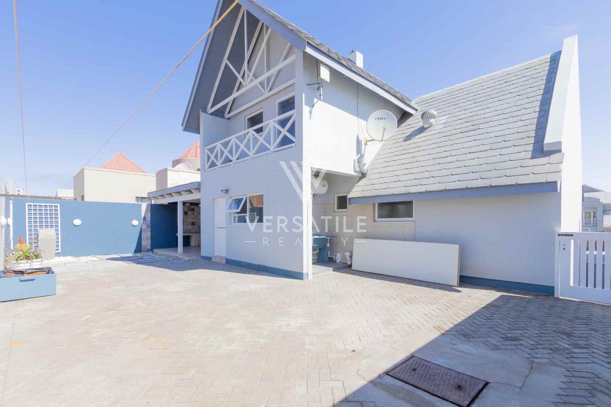 Rear exterior view of the property featuring a paved courtyard, a built-in braai area, and a balcony on the upper level.