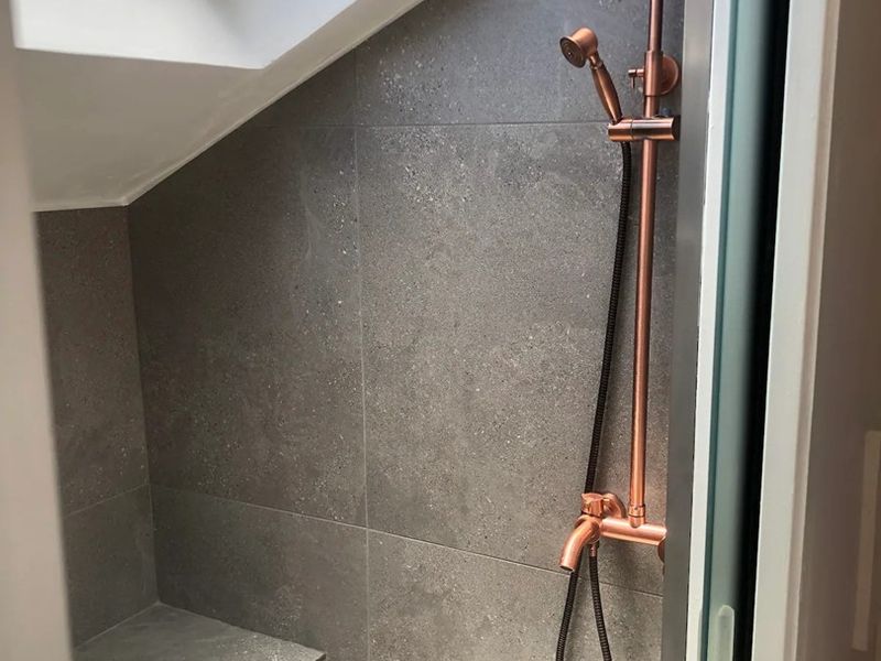 A modern shower enclosure featuring dark grey tiling, a built-in bench, and stylish copper fixtures, illuminated by a skylight.