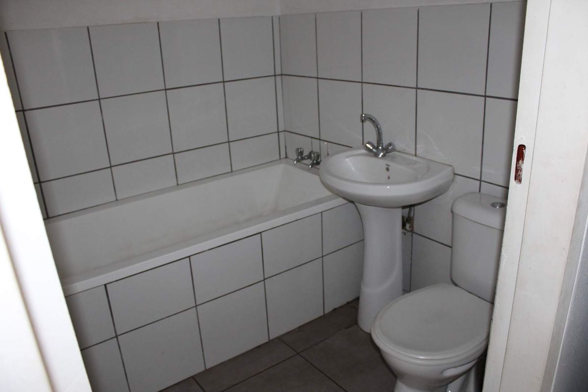 A functional bathroom featuring a standard bathtub, pedestal basin, and toilet with white wall tiling and grey floor tiles.