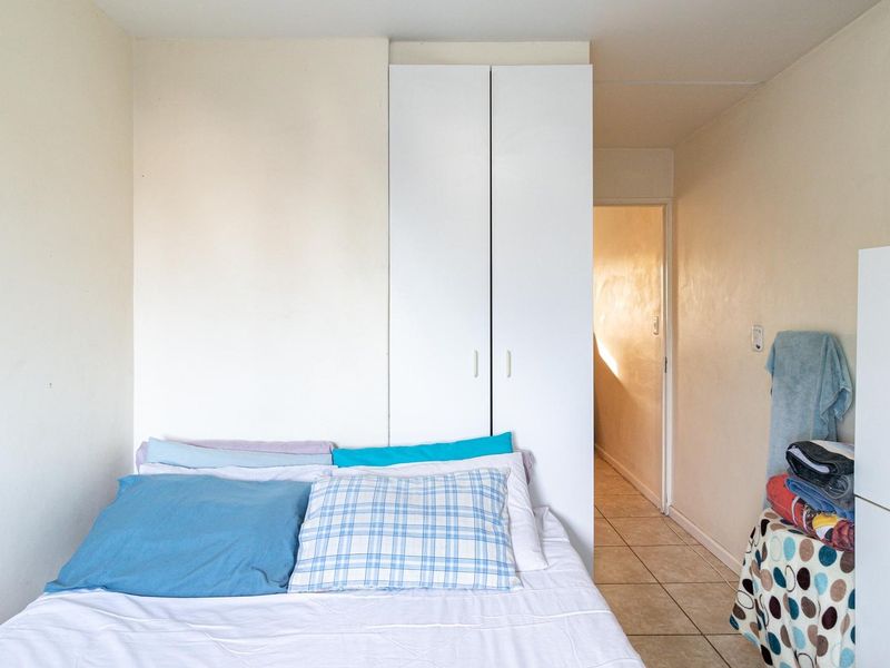 A bedroom featuring tiled flooring and a built-in white wardrobe, providing functional storage space within the apartment.