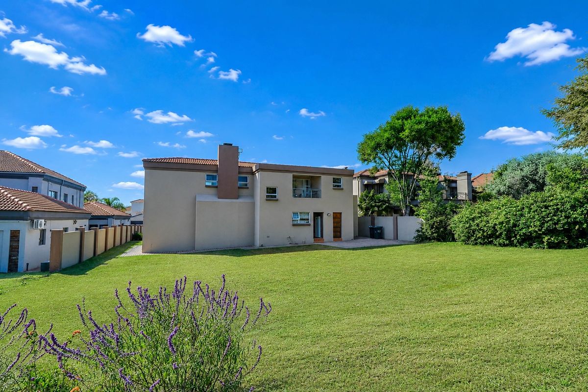 Rear view of a two-story residential property featuring a spacious lawn, paved patio area, balcony, and established boundary walls.