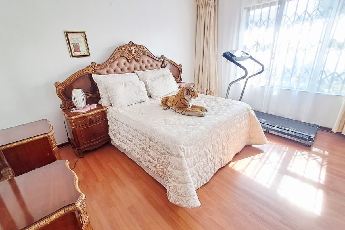 A spacious bedroom featuring laminate flooring and large windows fitted with security gates, offering natural light and a functional layout.