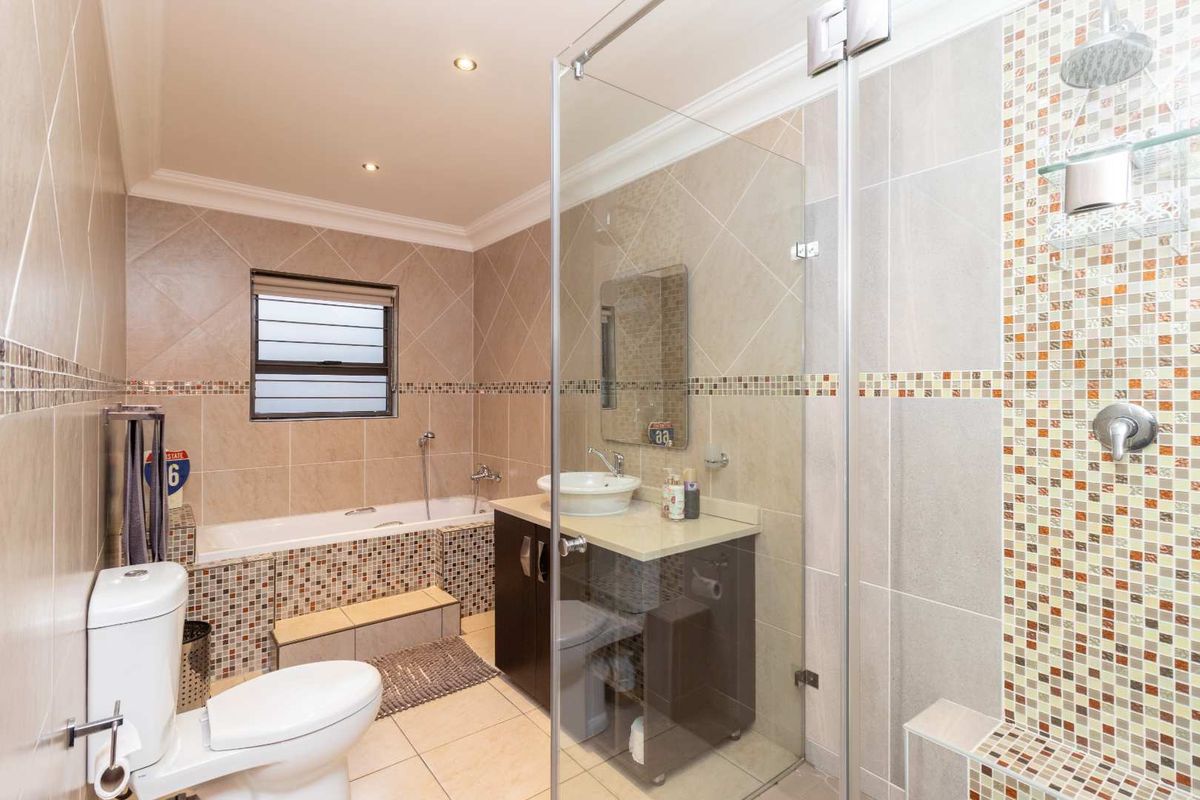 Modern bathroom featuring a glass-enclosed shower, a built-in bathtub with mosaic tile accents, a vanity with a vessel sink, and neutral wall tiling.