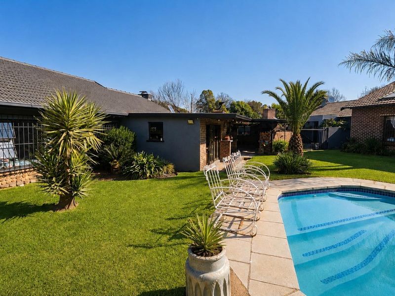 A well-maintained backyard featuring a swimming pool with tiled surround, manicured lawn, and a built-in outdoor braai area.