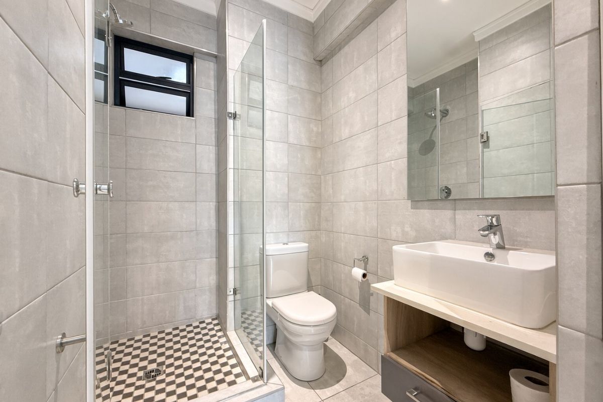 Modern bathroom featuring a glass-enclosed shower, contemporary vanity with basin, and neutral floor-to-ceiling tiling.