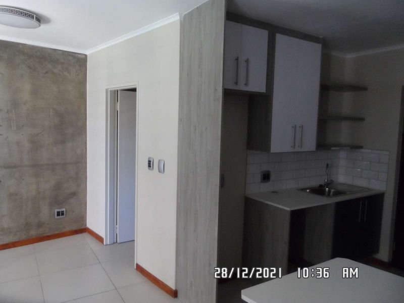 A compact kitchen area featuring modern two-tone cabinetry, a subway tile backsplash, and an exposed concrete feature wall, presented in a clean, empty space.