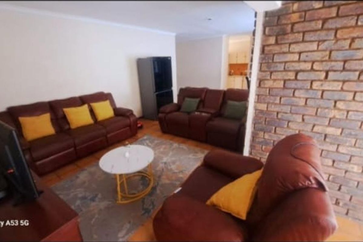 A living room area featuring a prominent exposed brick feature wall and tiled flooring, with an open-plan layout leading toward the kitchen.