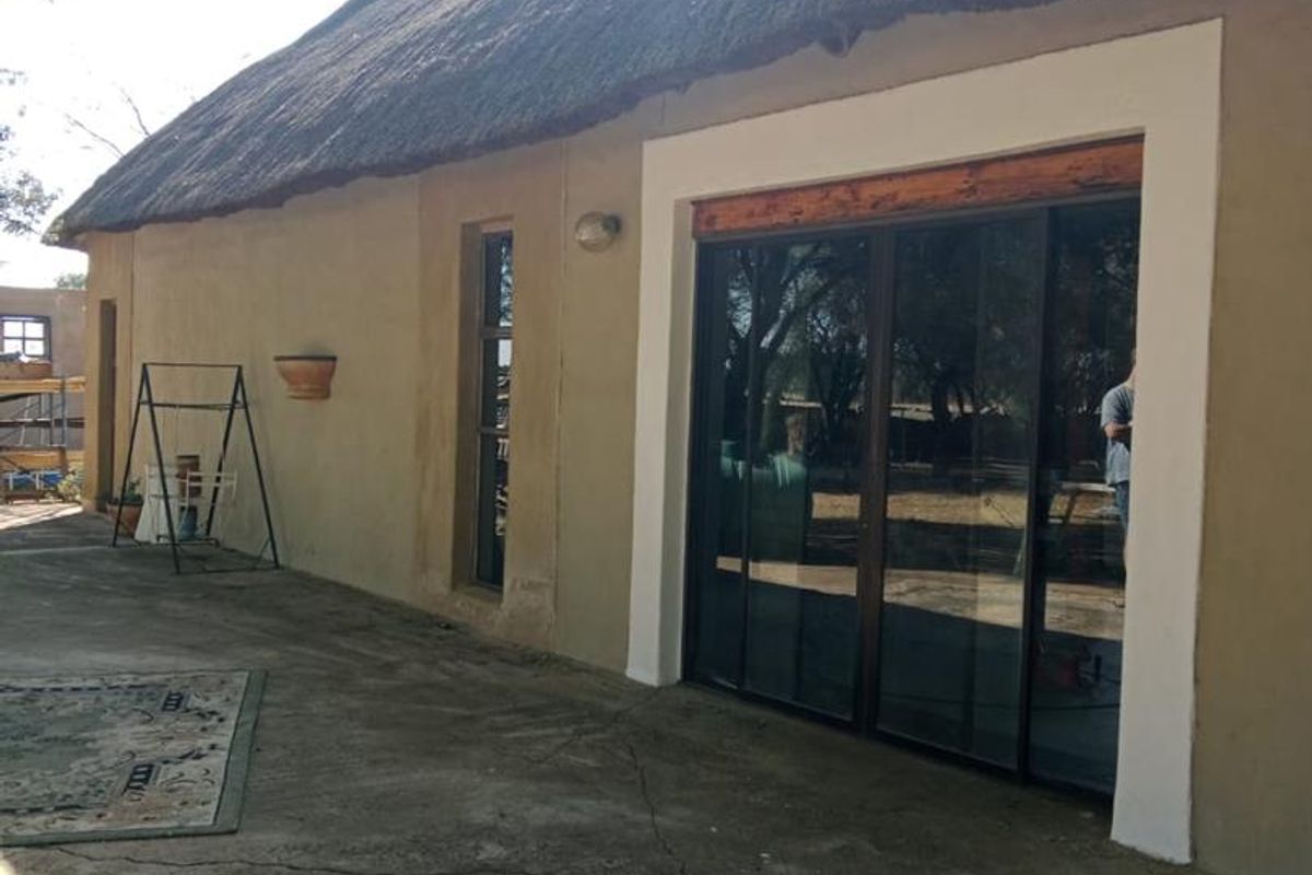 Exterior view of a small holding dwelling featuring a traditional thatched roof, concrete patio area, and modern sliding glass doors.