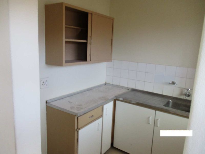 A compact, dated kitchen area featuring basic built-in cabinetry, a stainless steel sink, and a tiled splashback, currently in need of modernization.