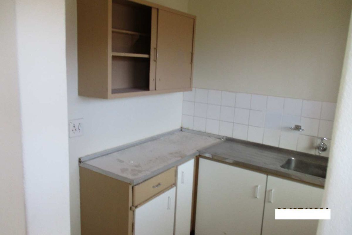 A compact, dated kitchen area featuring basic built-in cabinetry, a stainless steel sink, and a tiled splashback, currently in need of modernization.