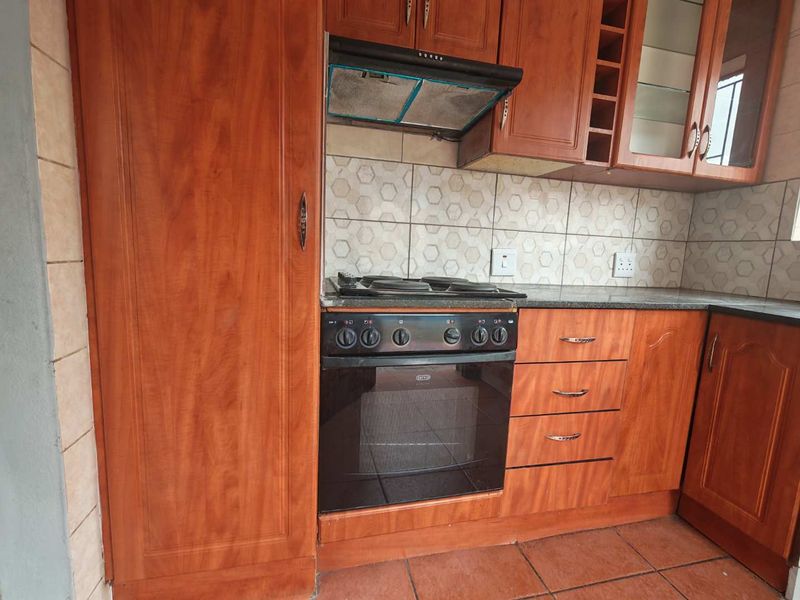 A functional kitchen featuring wood-finish cabinetry, granite countertops, a built-in oven with hob, and a tiled backsplash.