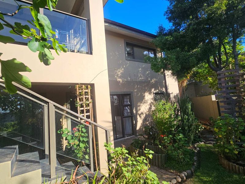 Rear view of the property featuring a landscaped garden, tiled staircase with glass balustrade, and access to the home via sliding glass doors.
