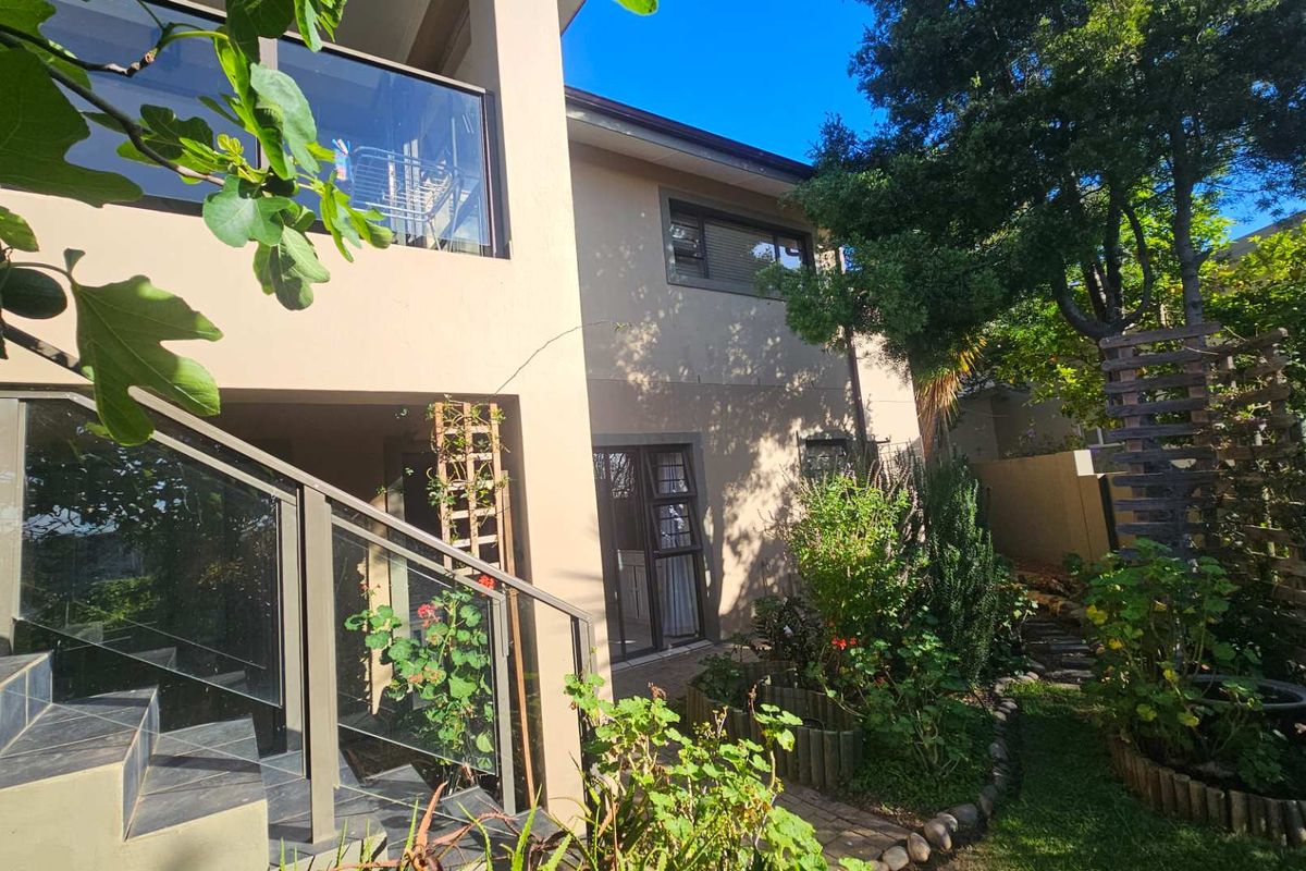 Rear view of the property featuring a landscaped garden, tiled staircase with glass balustrade, and access to the home via sliding glass doors.