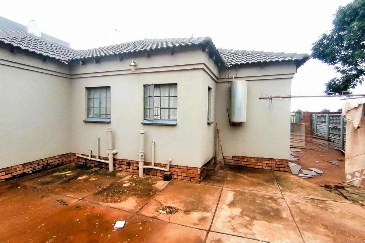 Rear exterior view of the property featuring a concrete patio area, exposed plumbing, and a wall-mounted geyser.