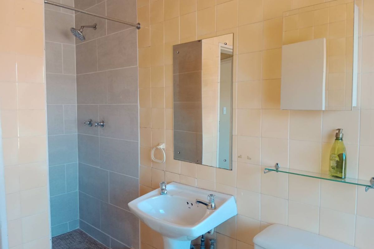 A functional bathroom featuring a pedestal basin, toilet, and a shower area with a mix of beige and grey wall tiles.