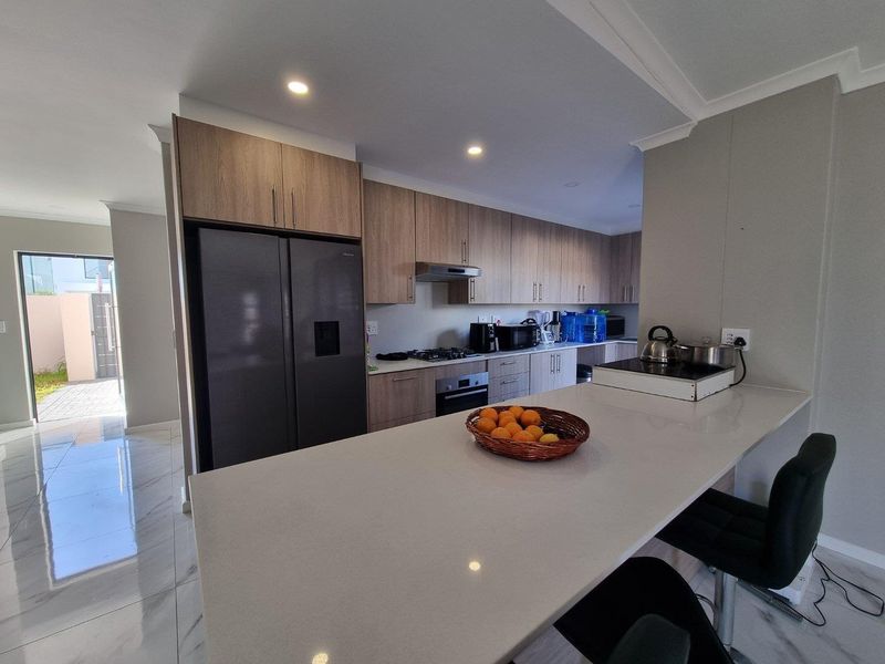Modern kitchen featuring wood-finish cabinetry, stone countertops, a breakfast bar, and integrated appliances, complemented by sleek tiled flooring and recessed lighting.