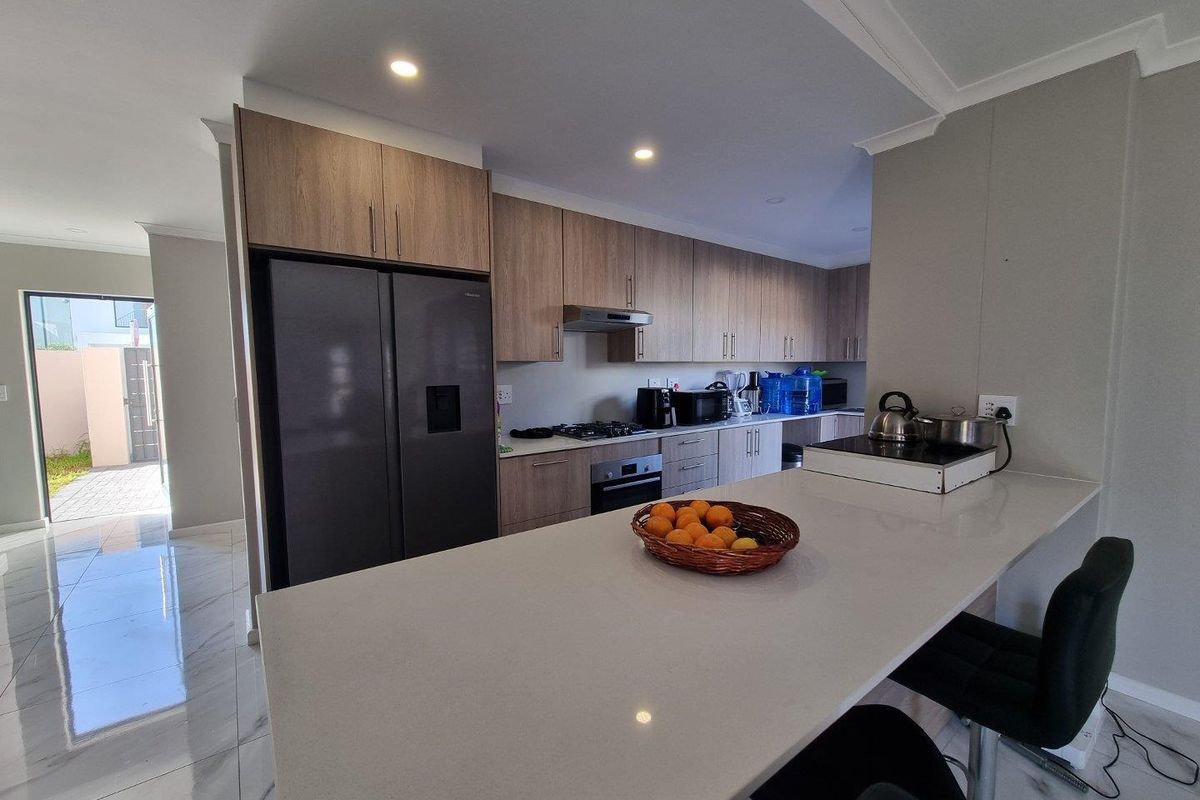 Modern kitchen featuring wood-finish cabinetry, stone countertops, a breakfast bar, and integrated appliances, complemented by sleek tiled flooring and recessed lighting.