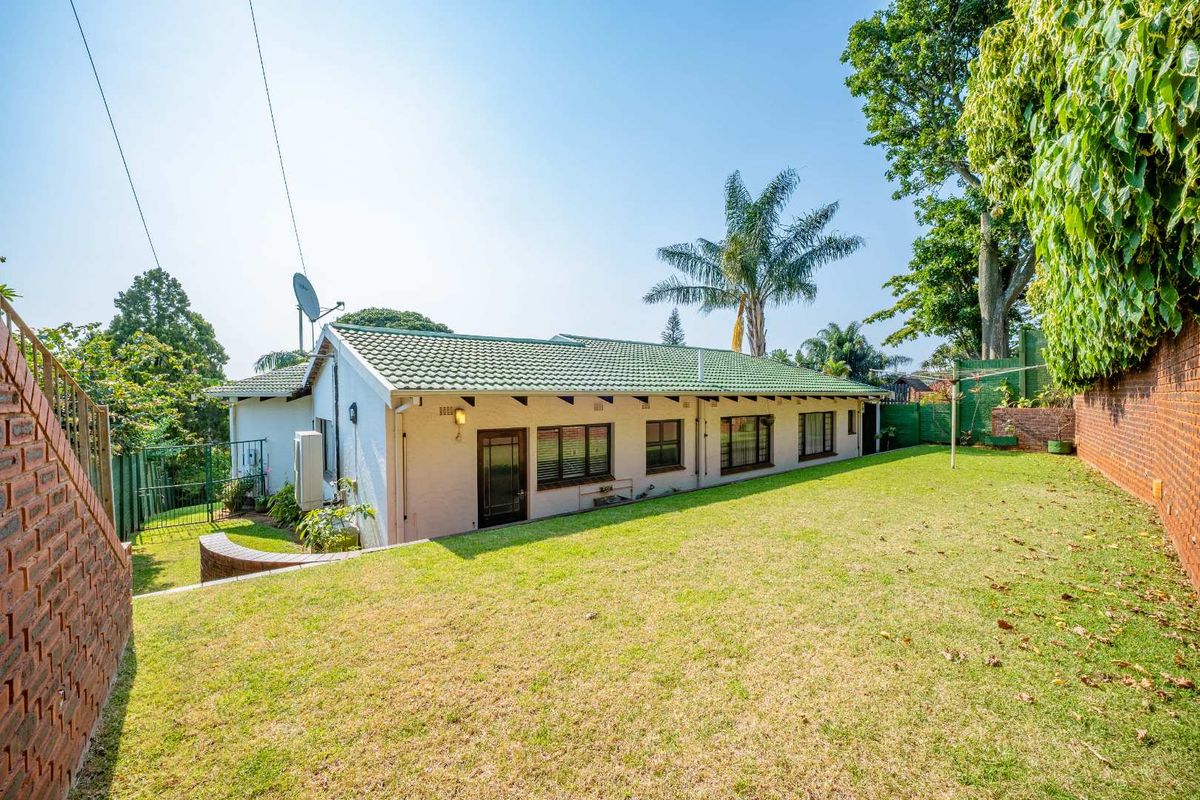Rear view of the house featuring a tiled roof, white exterior walls, and a spacious grass garden enclosed by brick boundary walls.