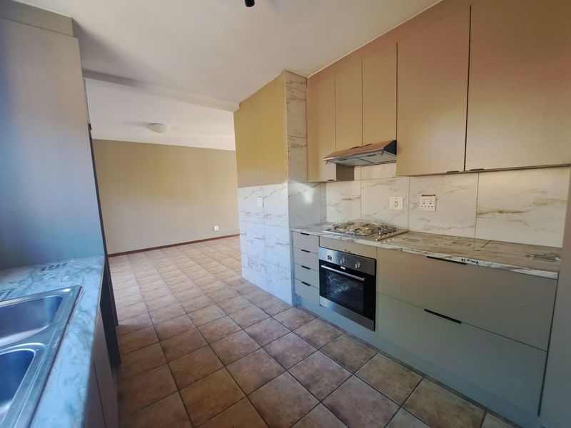 Open-plan kitchen area featuring modern cabinetry, marble-look splashbacks, built-in oven, gas hob, and tiled flooring, flowing into an adjacent living space.
