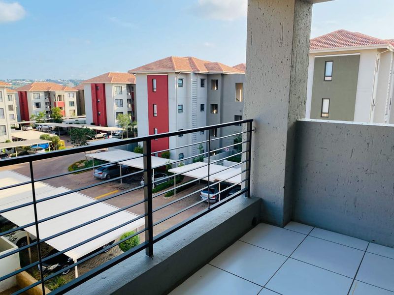A clean, tiled balcony featuring a metal balustrade, offering an elevated view over the apartment complex parking area.