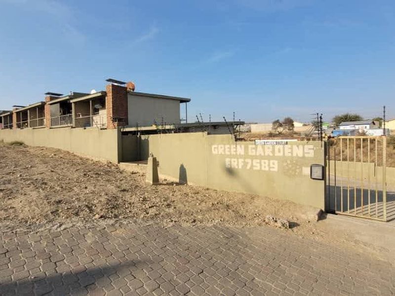 Exterior view of the Green Gardens apartment complex featuring a perimeter wall with electric fencing, gated entrance, and paved driveway access.