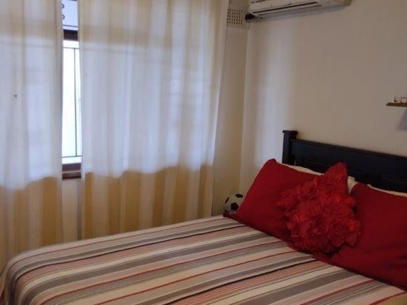 A functional bedroom featuring a wall-mounted split-system air conditioning unit and a window with curtains.